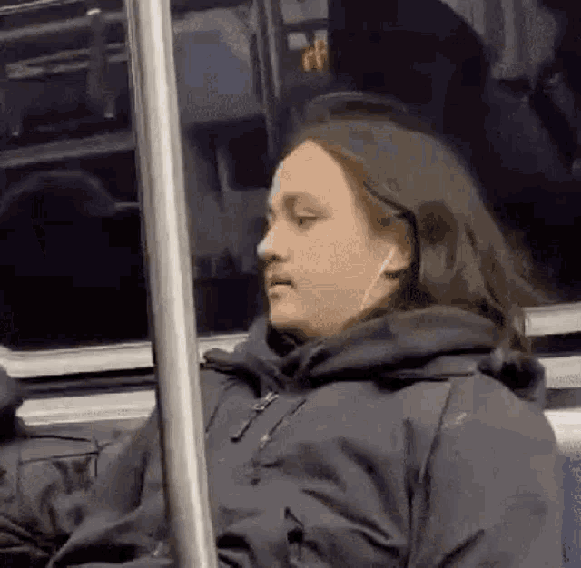a woman is sitting on a bus wearing headphones and looking out the window .