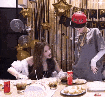 a man and a woman are sitting at a table with a cake and coca cola cans .