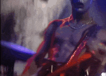 a shirtless man is playing a guitar in a dark room