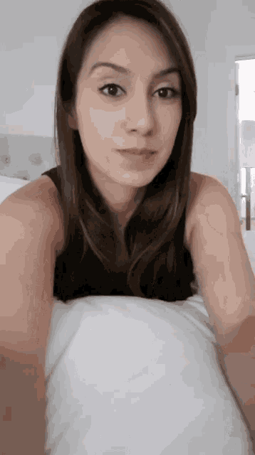 a woman in a black tank top is taking a selfie in bed