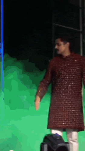 a man in a maroon shirt is standing in front of a green screen