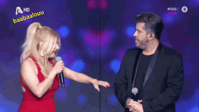 a woman in a red dress is singing into a microphone next to a man in a black suit
