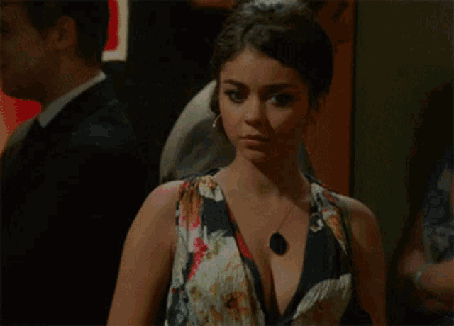a woman in a floral dress has a black pendant on her neck