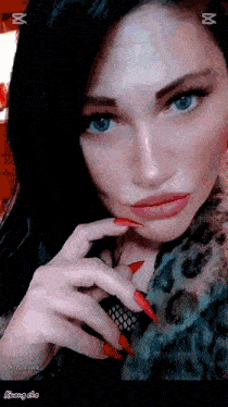 a woman with long red nails is wearing a leopard print coat and looking at the camera