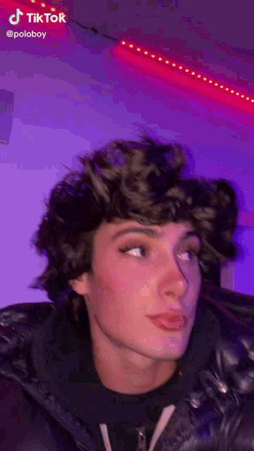 a young man with curly hair is standing in front of a red light .