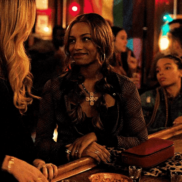 a woman is sitting at a bar talking to another woman and smiling