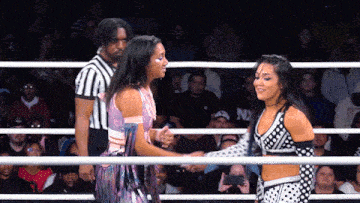 two women shaking hands in a wrestling ring with a referee