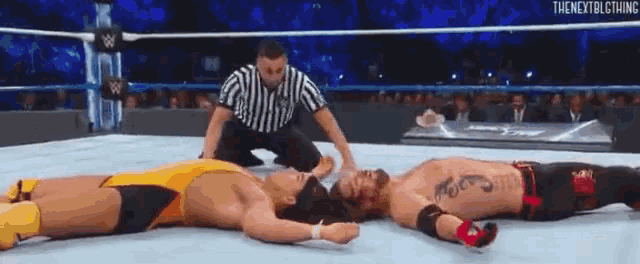 three wrestlers are laying on the ground in a wrestling ring with a referee .