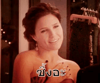 a woman in a red dress is smiling and holding her hands to her chest in a room with clothes hanging on a rack .