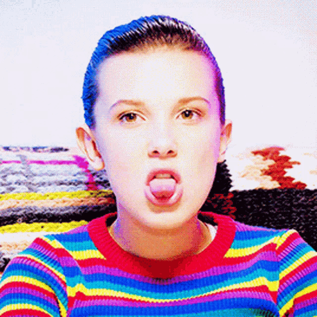 a woman in a rainbow striped sweater is sticking her tongue out
