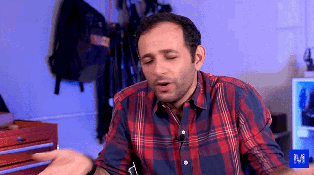 a man wearing a plaid shirt is sitting in front of a blue m sign