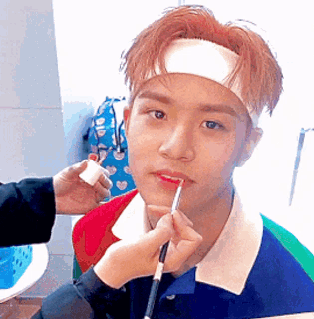 a young man wearing a headband is getting lipstick applied to his lips