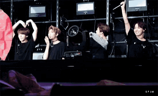 a group of young men are making a heart shape with their hands while sitting on a stage .