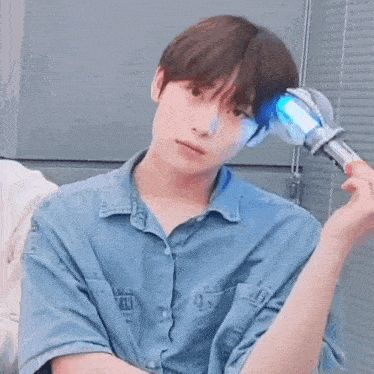 a young man in a denim shirt is holding a blue light stick .