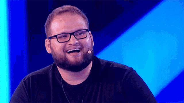 a man with glasses and a beard is laughing in front of a microphone