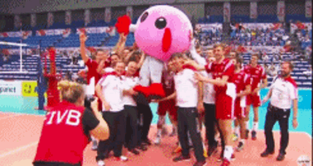 a group of volleyball players are posing for a photo with a pink mascot .