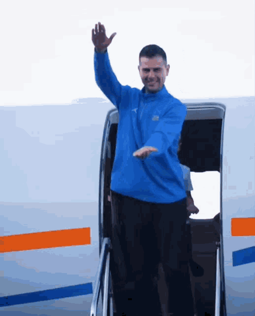 a man in a blue sweater is waving from the door of a plane