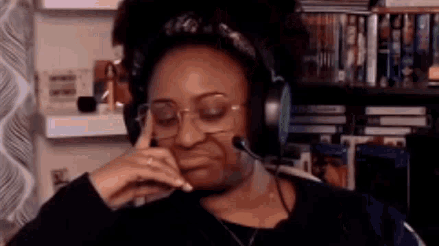 a woman wearing headphones and glasses is making a funny face while sitting in front of a bookshelf .