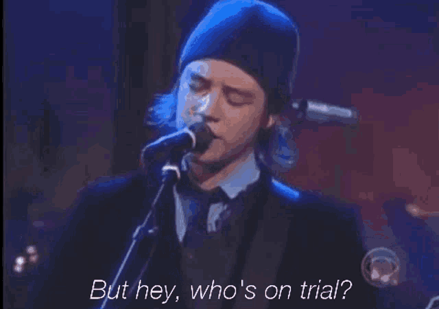 a man singing into a microphone with the words but hey who 's on trial next to him