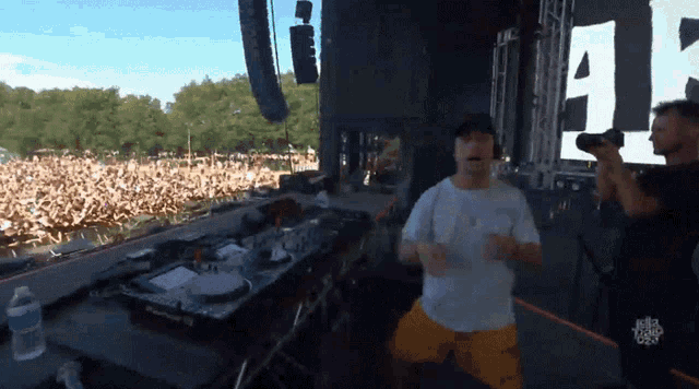 a man in a white shirt is dancing in front of a crowd at a concert with the letter a on the screen behind him