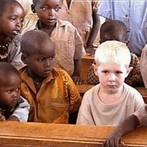a group of children are sitting at desks in a classroom looking at the camera .