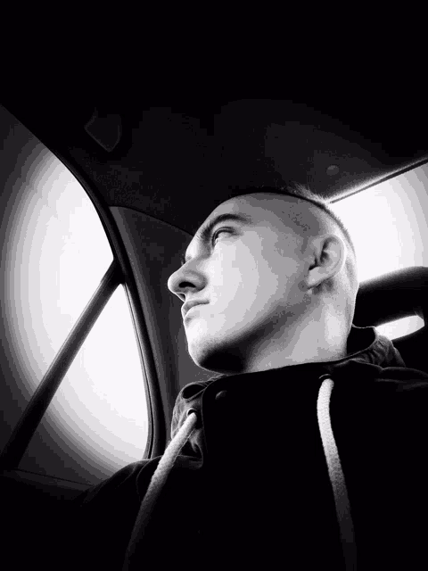 a man with a shaved head is looking out a car window
