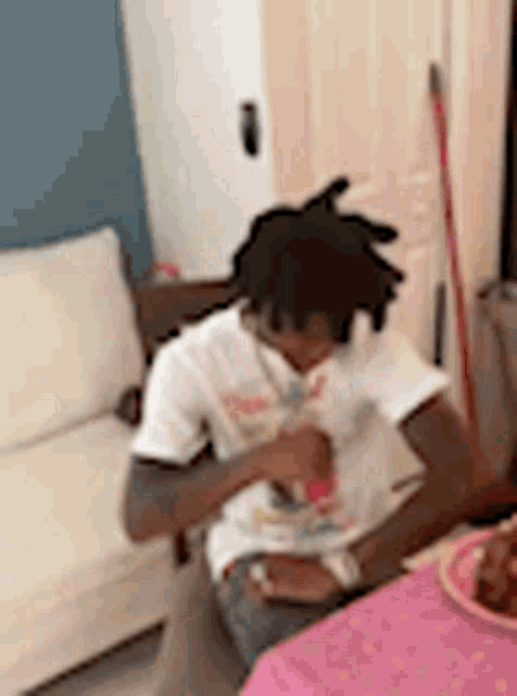 a man is sitting at a table with a plate of food and a couch in the background .