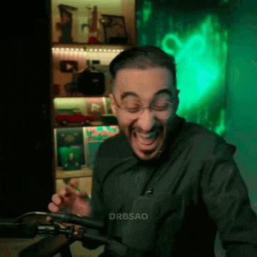 a man with glasses is sitting in front of a microphone and laughing .