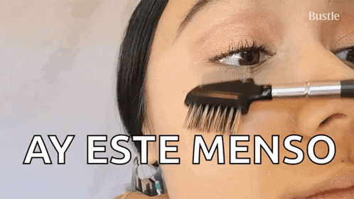 a woman is brushing her eyebrows with a brush and the words ay este menso are above her face .