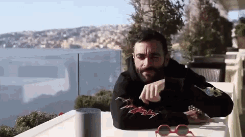 a man with a beard is sitting at a table with a speaker and sunglasses .