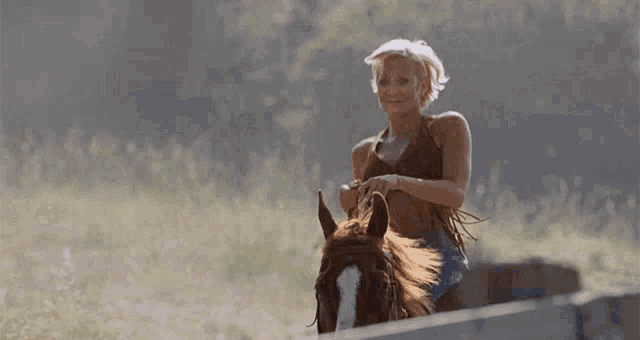 a woman is riding a horse in a field and smiling at the camera .