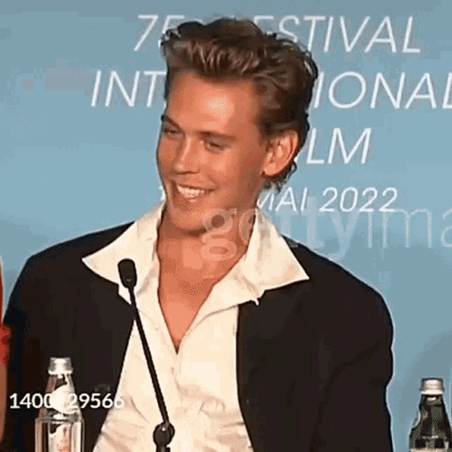 a man in a suit and white shirt is sitting at a table with a microphone and smiling .
