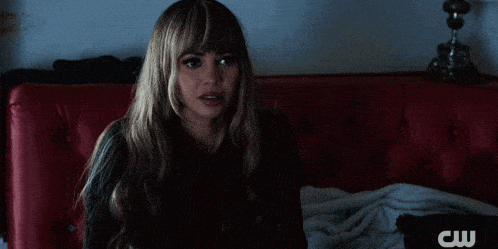 a woman sits on a red couch with a cw logo on the bottom