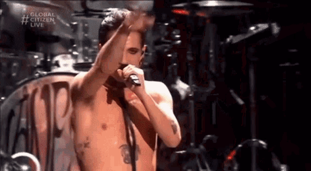 a shirtless man singing into a microphone with the words global citizen live on the bottom right