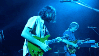 two men playing guitars on a stage with a blue light behind them