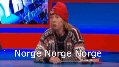 a man wearing a red hat and sweater is sitting at a table with the words norge norge norge written in white letters