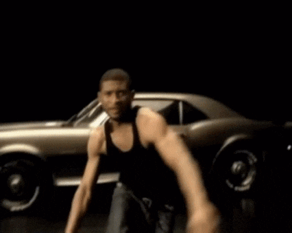 a man in a black tank top is dancing in front of a silver car .