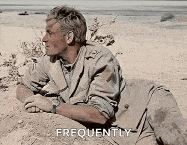 a man in a trench coat is laying in the sand on a beach .