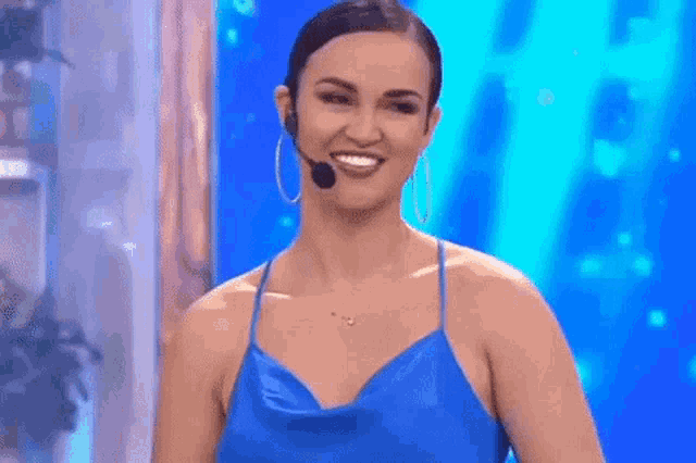 a woman in a blue dress is smiling and wearing a microphone .