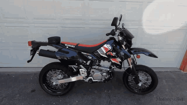 a black suzuki dirt bike is parked in front of a garage