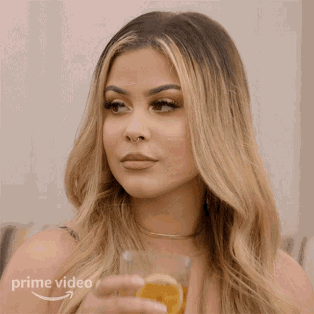 a woman holding a glass of orange juice with a prime video arrow in the corner
