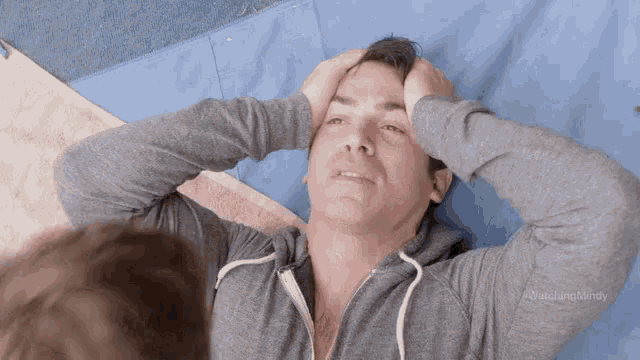 a man is laying on a blue mat holding his head .