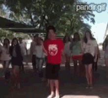 a man in a red shirt with a panda on it stands in front of a crowd of people .