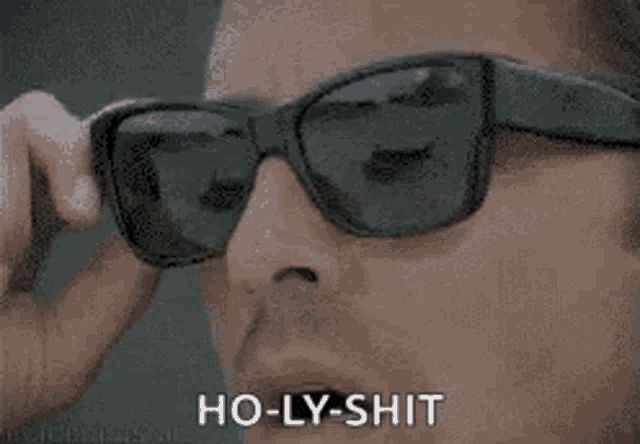 a man wearing sunglasses is saying ho-ly-shit while looking at something .