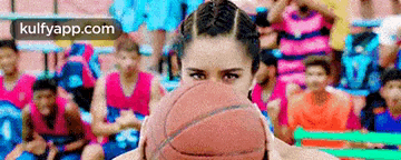 a woman is holding a basketball in front of her face in front of a crowd of people .