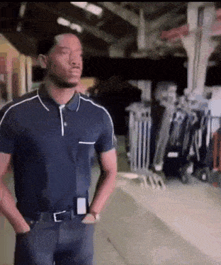 a man in a blue polo shirt is standing in a warehouse with his hands in his pockets