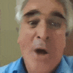 a man with gray hair and a blue shirt is making a funny face with his mouth open .