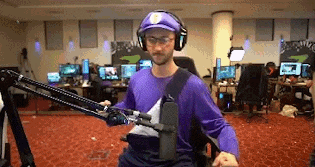 a man in a purple shirt and hat is standing in a room with a microphone .