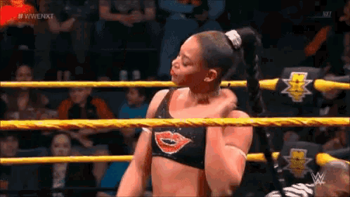 a female wrestler is standing in a wrestling ring with a crowd watching .