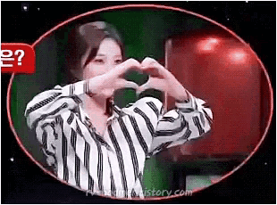 a woman is making a heart shape with her hands in a striped shirt .